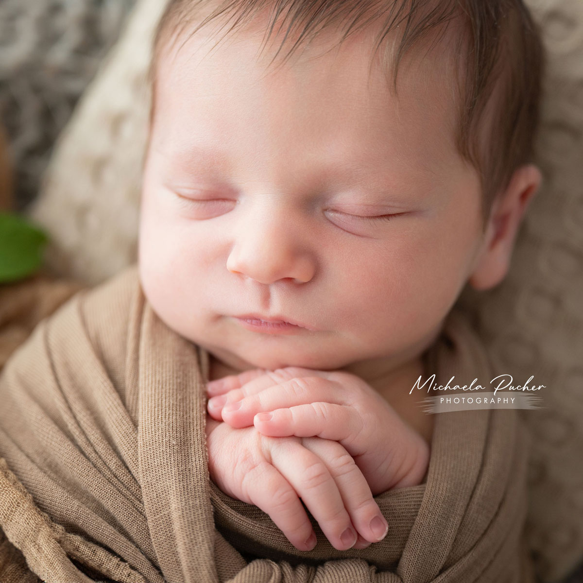 Nahaufnahme eines schlafenden Neugeborenen mit gefalteten Händen unter dem Kinn, eingewickelt in braune Tücher